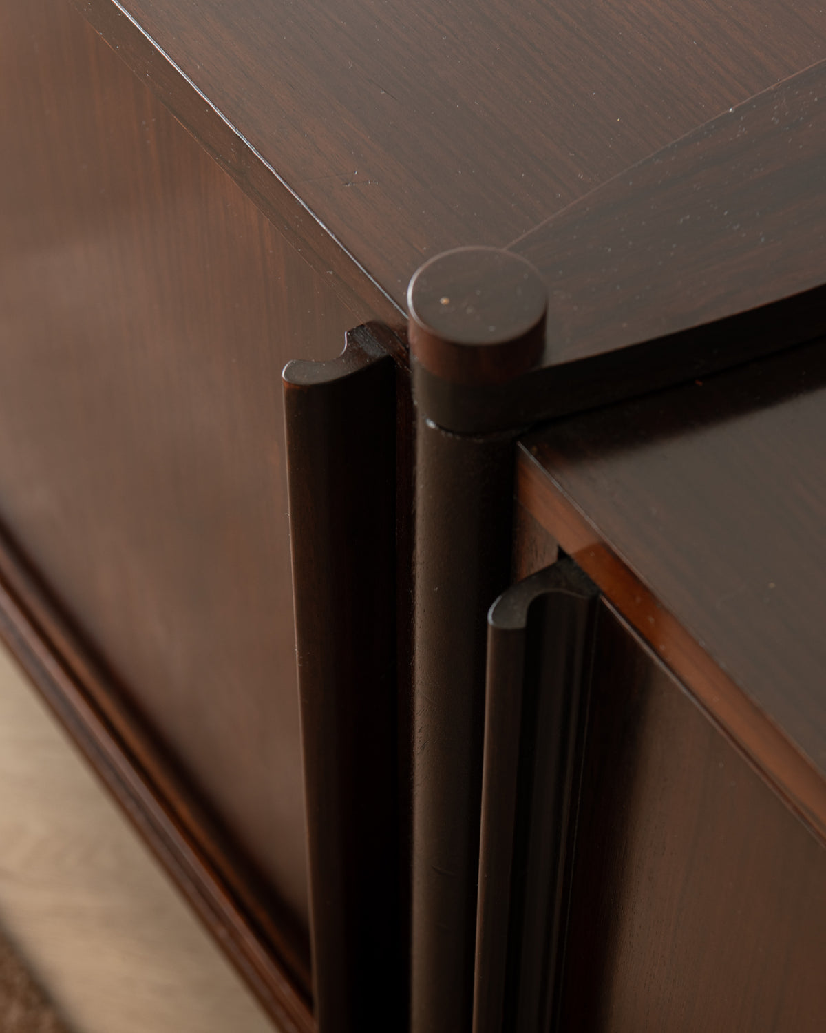 Close-up detail of a dark brown wooden cabinet with a dark metal cylindrical pull handle and matching drawer pulls.