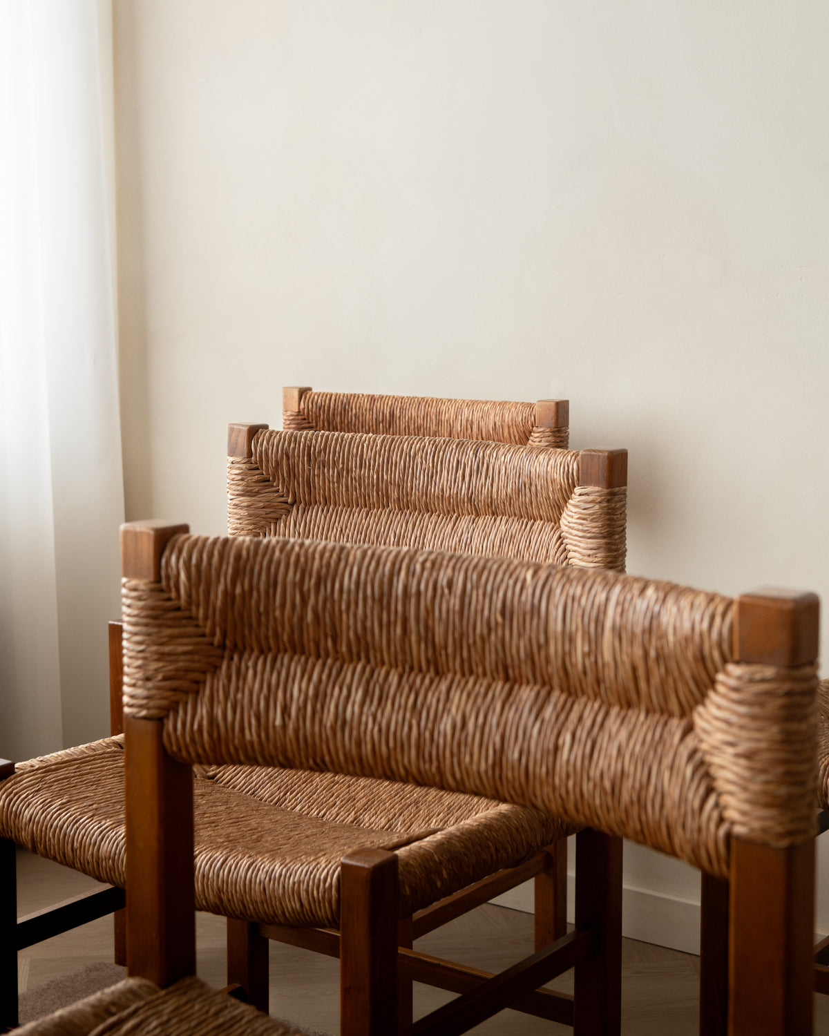 Three wooden armchairs with woven natural-fiber seats and backs, arranged against a plain off-white wall.