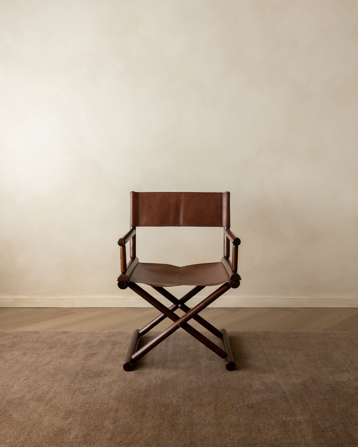 A classic brown leather and wood folding director's chair with casters, set against a neutral beige wall and carpeted floor.