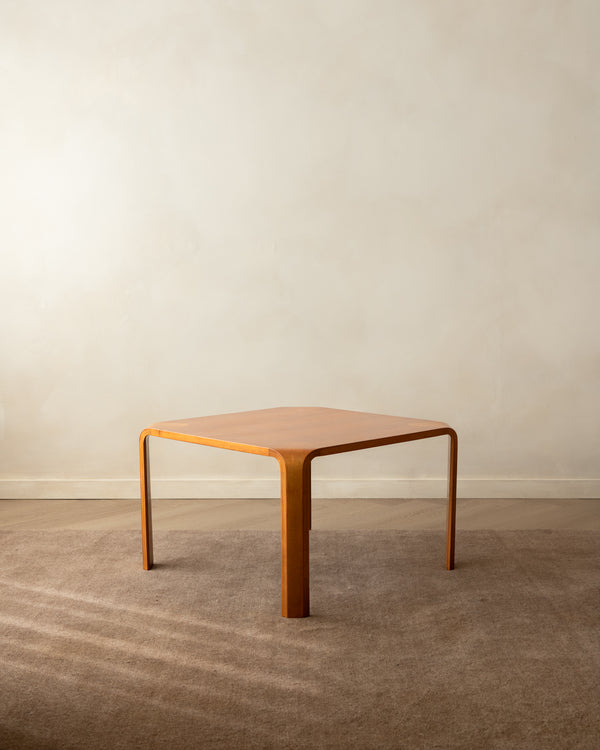 A mid-century modern wooden coffee table with a hexagonal top and curved legs, set on a textured brown carpet against a neutral beige wall.